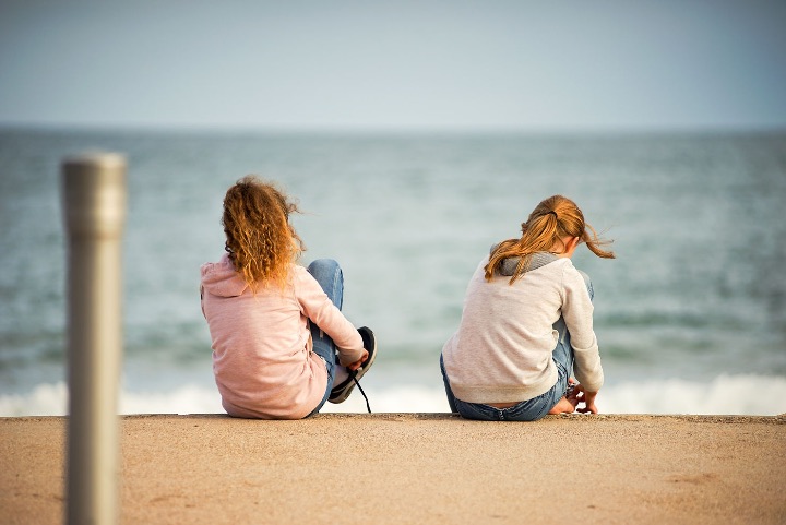 Two children sitting on a quayside looking out to sea